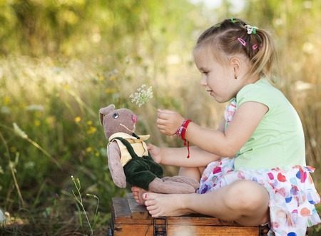Summer outdoor portrait of cute little girl sitting on meadow with old suitcase with toysの写真素材