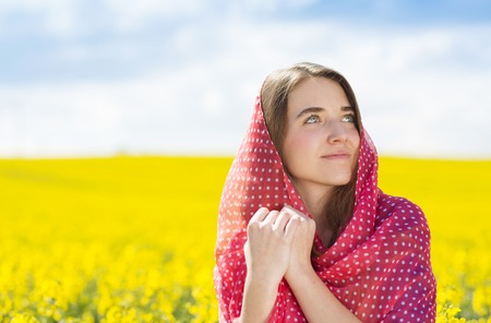 Happy young girl with red scarf enjoying free time in yellow colza fieldの写真素材