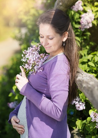 Outdoor portrait of beautiful pregnant woman holding her belly and bunch of flowersの写真素材