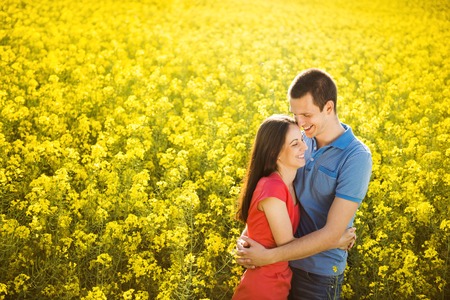 Happy young couple in love hugging in yellow colza fieldの写真素材