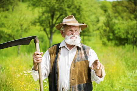 Old farmer with scythe taking a break from mowing the grassの写真素材