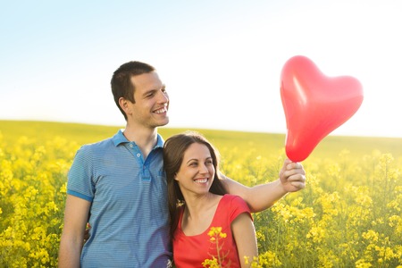 Happy young couple in love with heart shaped baloon in yellow colza fieldの写真素材