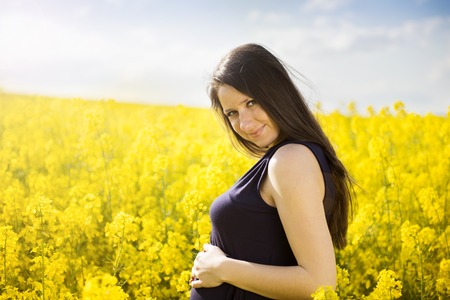 Outdoor portrait of beautiful pregnant woman posing in yellow colza fieldの写真素材