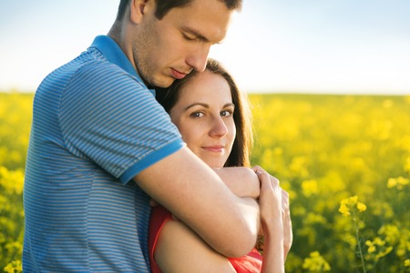 Happy young couple in love hugging in yellow colza fieldの写真素材