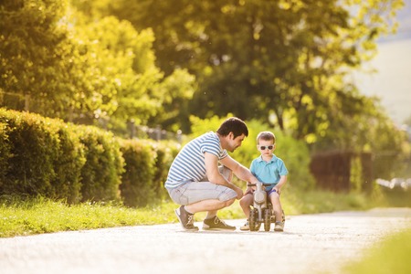 Young father with his little son on motorbike in green sunny parkの写真素材