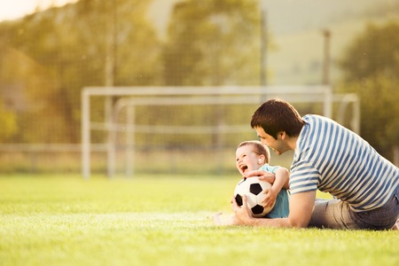 Young father with his little son playing football on football pitch Young father with his little son playing football on football pitch