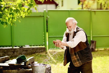 Old farmer is washing his face with water from bucketの写真素材