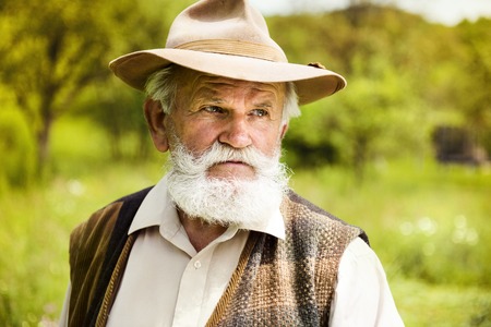 Portrait of old farmer with beard and hat in his backyardの写真素材