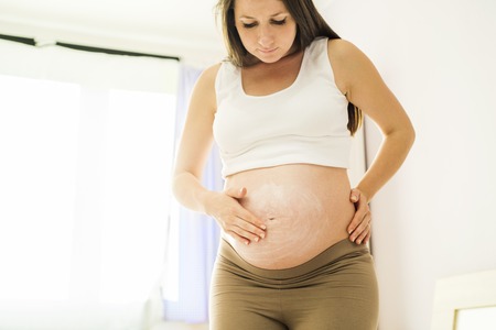 beautiful pregnant woman applying anti stretch mark cream or moisturizer