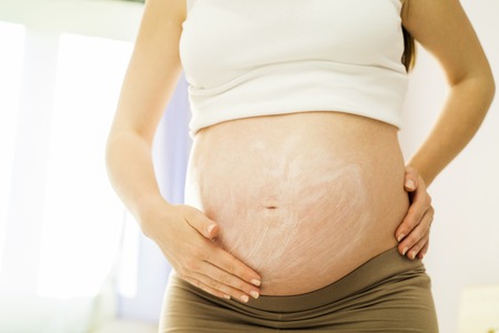 beautiful pregnant woman applying anti stretch mark cream or moisturizer
