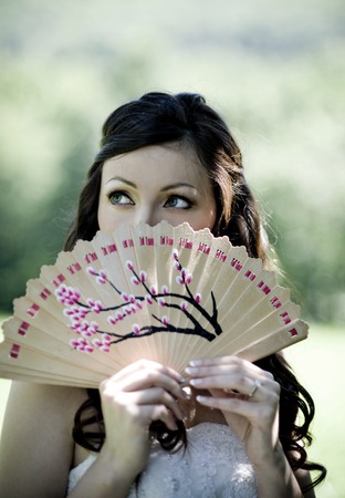 Bride in white wedding dress and summer fan posing at the meadowの写真素材