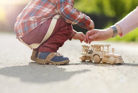 Close-up of little boy playing with wooden tractor on pavement outsideの写真素材