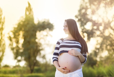 Outdoor portrait of beautiful pregnant woman holding her bellyの写真素材