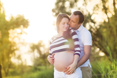Happy young pregnant couple hugging in natureの写真素材