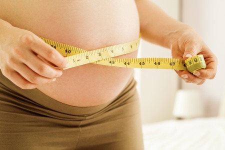 Portrait of unrecognizable pregnant woman measuring her belly with tape measureの写真素材