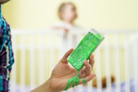 Closeup of father holding damaged mobile phone and his little daughter in backgroundの写真素材