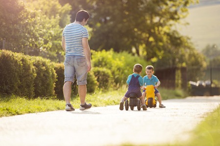 Young father with his little sons on motorbikes in green sunny parkの写真素材