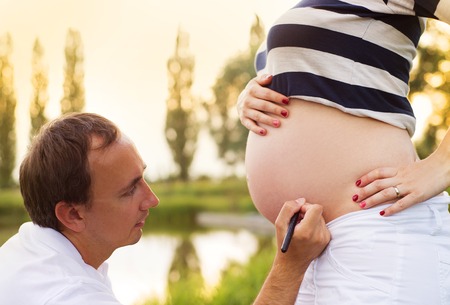 Man is writing a name on pregnant woman s belly in natureの写真素材