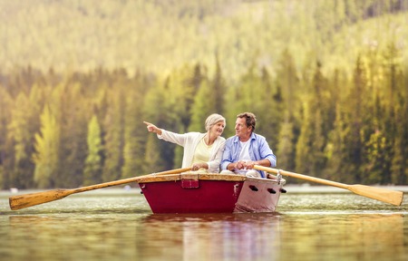 Senior couple paddling on boat with mountains in backgroundの写真素材