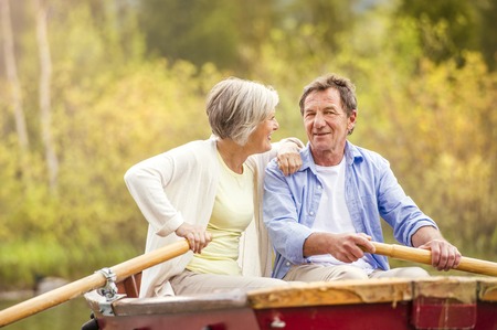 Senior couple paddling on boat with mountains in backgroundの写真素材
