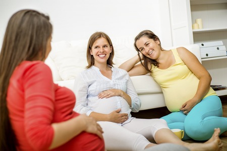Three pregnant women sitting in front of sofaの写真素材