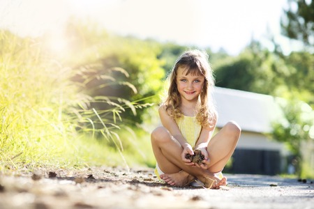 Cute little girl sittting and holding pine cones outdoorsの写真素材