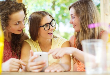 Three beautiful girls drinking and having fun with smartphone in pub gardenの写真素材