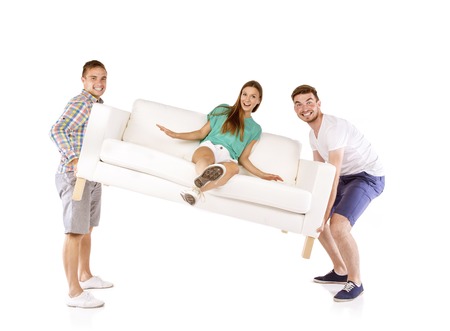 Two young handsome men lifting sofa with young beautiful woman sitting on it, isolated on white...