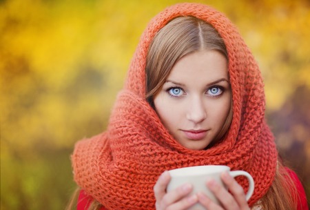 Portrait of beautiful girl with scarf and cup with hot drink in autumn natureの写真素材