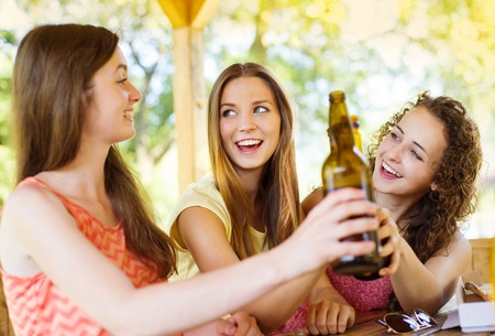 Three happy friends drinking beer, chatting and having fun in pub gardenの写真素材