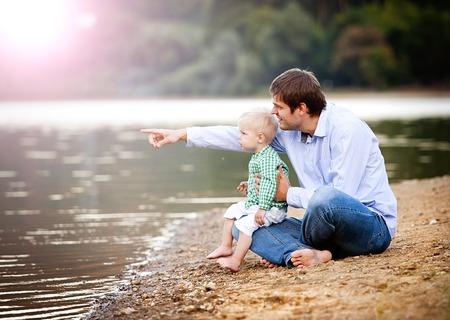 Happy young father spending time together with his little sonby the lake on the sandy beachの写真素材