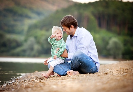 Happy young father spending time together with his little sonby the lake on the sandy beachの写真素材