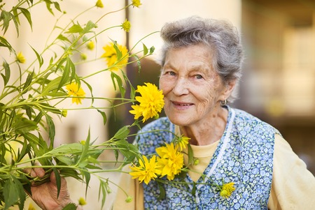 Portrait of senior woman in apron with yellow flower in the sunny garden