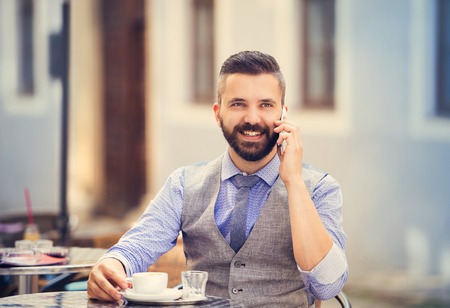 Modern hipster businessman drinking espresso coffee in the city cafe during lunch time and calling by mobile phoneの写真素材