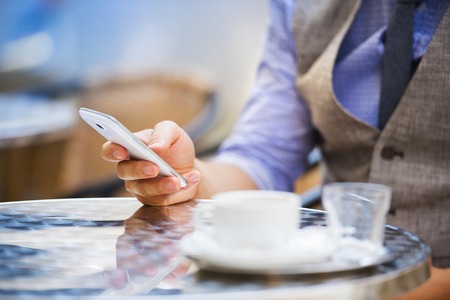 Detail of businessman drinking espresso coffee in the city cafe during lunch time and using mobile phoneの写真素材