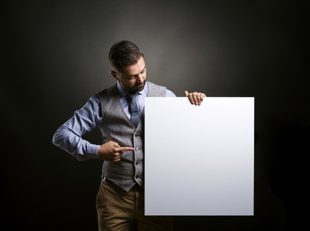 Studio shot of modern hipster businessman holding blank advertisement on black backgroundの写真素材