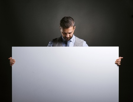 Studio shot of modern hipster businessman holding blank advertisement on black backgroundの写真素材