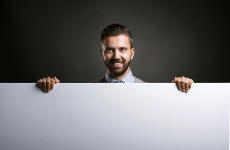 Studio shot of modern hipster businessman holding blank advertisement on black backgroundの写真素材