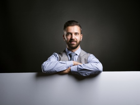 Studio shot of modern hipster businessman holding blank advertisement on black backgroundの写真素材