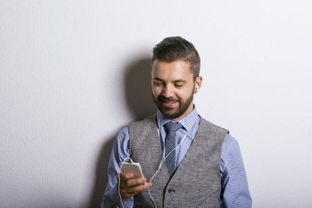 Studio shot of modern hipster businessman with headphones, listening to music from mobile phoneの写真素材
