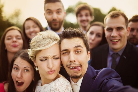 Young couple of newlyweds with group of their firends taking selfie and making funny grimaces