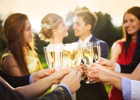 Wedding guests clinking glasses while the newlyweds hugging in the backgroundの写真素材