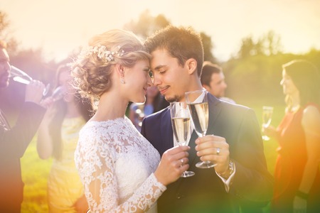 Young newlyweds clinking glasses and enjoying romantic moment together at wedding reception outside