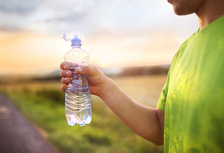 Cross-country trail running man having water break at sunsetの写真素材