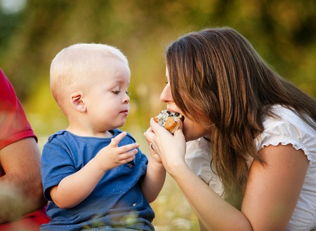 Cute little boy is feeding mother with muffin cake in natureの写真素材