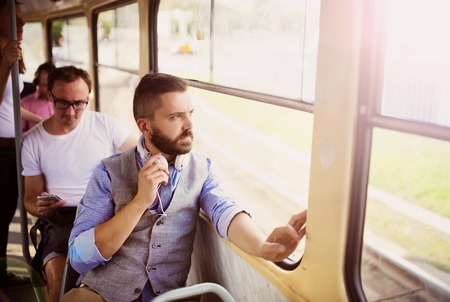 Handsome hipster modern man with headphones traveling by tram in townの写真素材