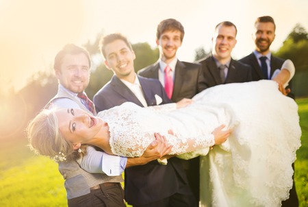 Outdoor portrait of young groom with his friends holding beautiful brideの写真素材