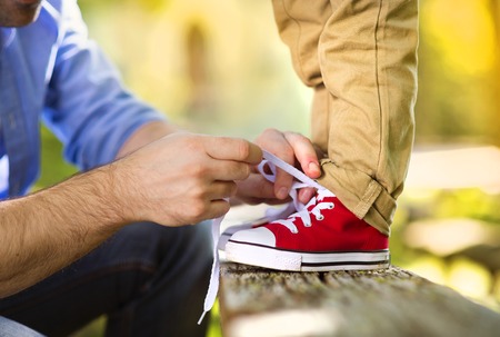 Father is helping his son to tie his shoes in summer nature Father is helping his son to tie his shoes in summer nature