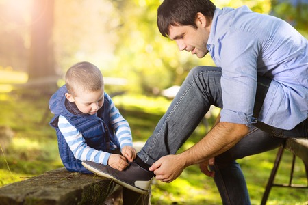 Father and son spending time together in summer nature, little boy is tying his father\'s shoesの写真素材
