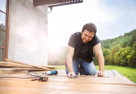 Smiling handyman installing wooden flooring in patio, working with hammerの写真素材